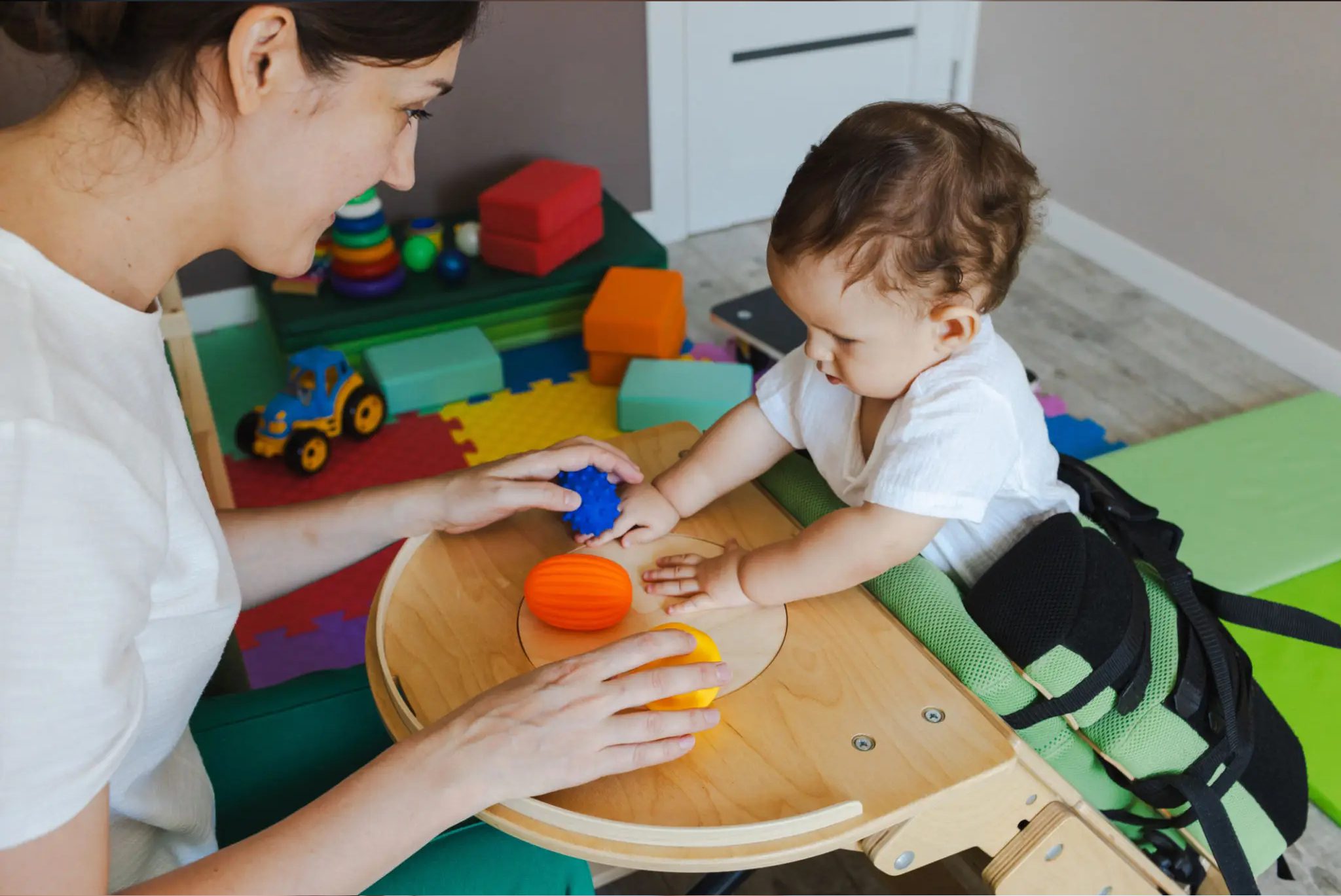 Caregiver helping baby play with colorful balls